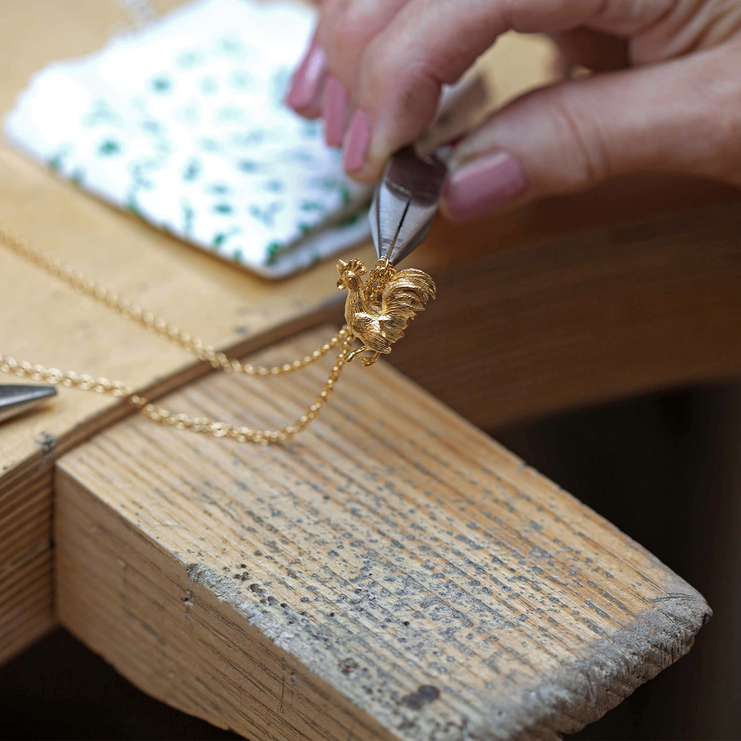 fairmined gold plated rooster necklace by Alex Monroe held in pliers in jewellery workshop