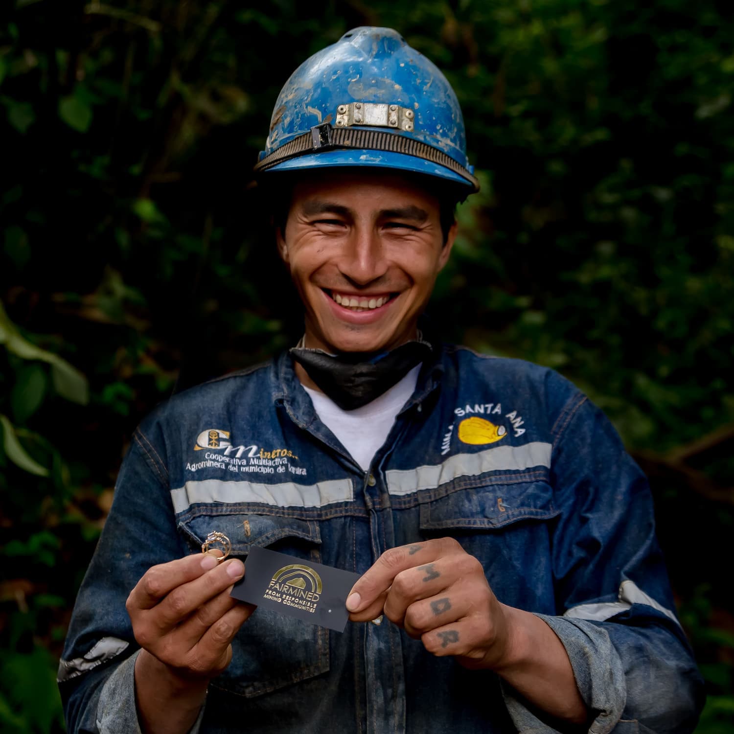 Fairmined Gold Miner wearing blue hard hat and overall and smiling holding fairmined gold rings