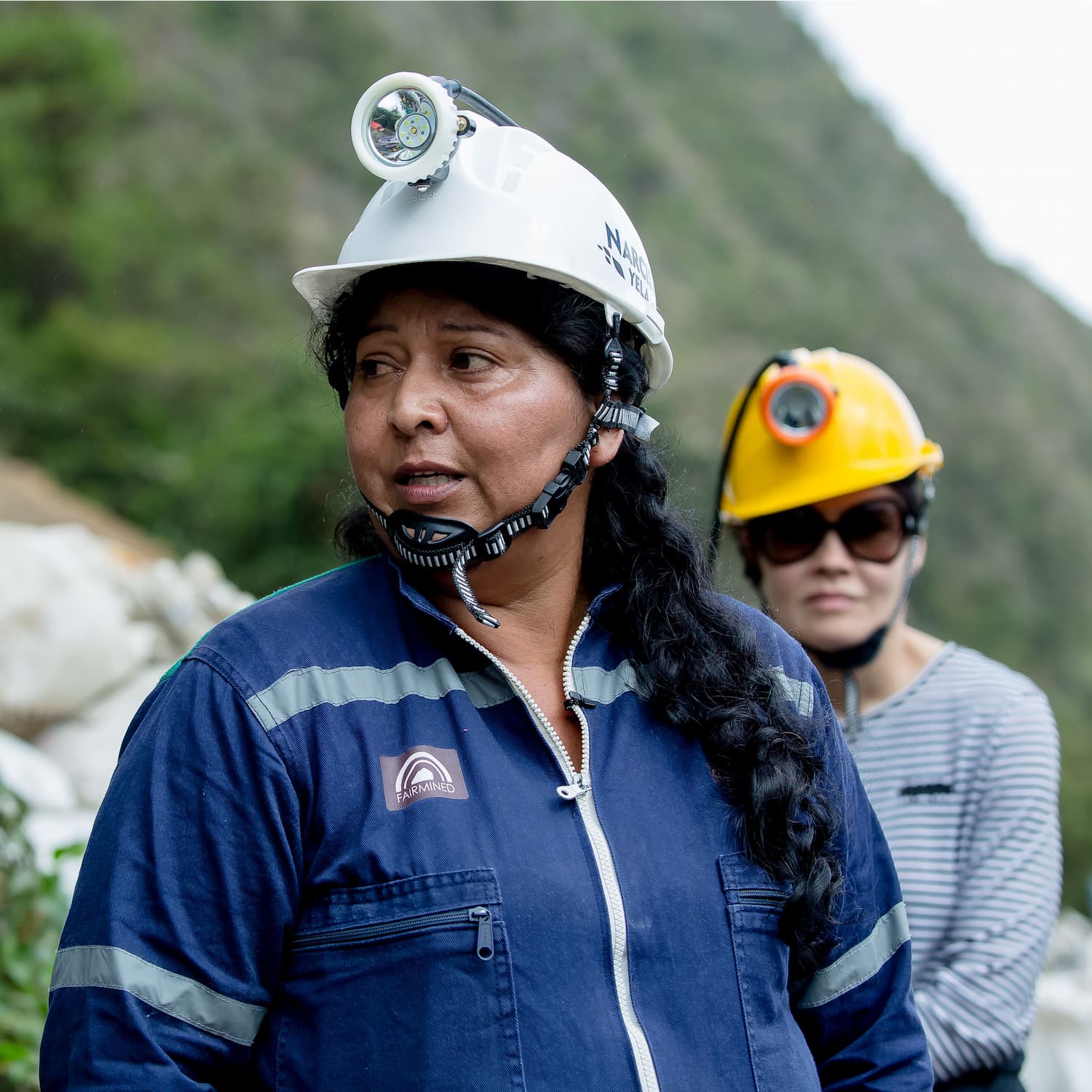 fairmined gold woman miner wearing hard hat with lamp and blue overall