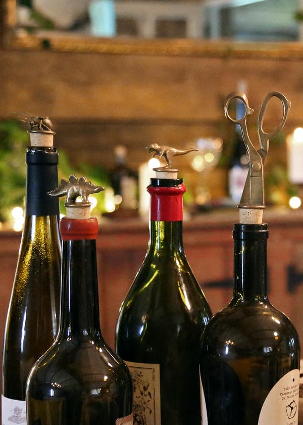 Festive hosting scene with a selection of bottle stoppers in use on wine bottles. A flying bee, Stegosaurus, T-rex and pair of scissors as the bottle stopper designs.