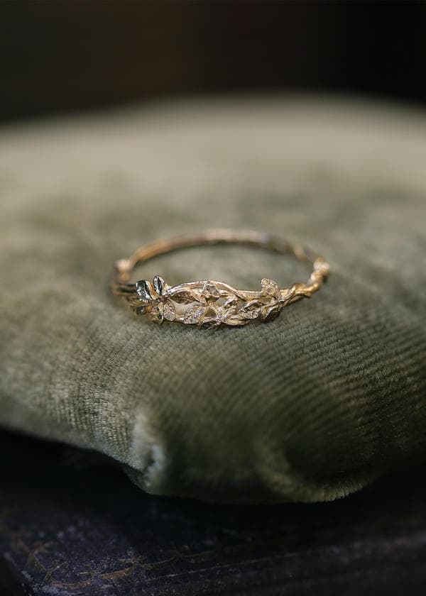 Solid gold vine and diamond ring on a dark green velvet cushion.