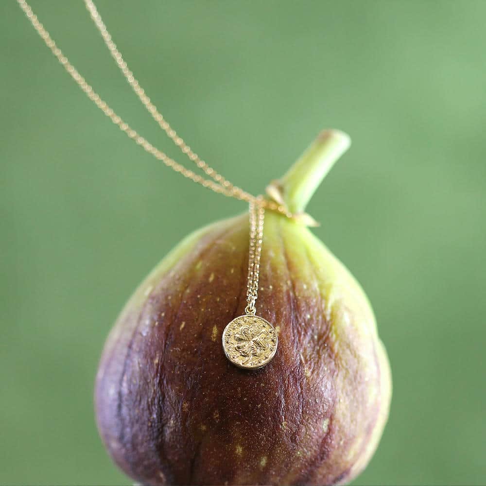 Teeny Tiny Lucky Penny necklace displayed on a green fix against a green backdrop.