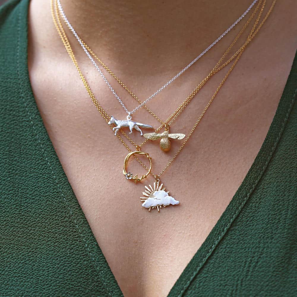 Woman wearing four layered necklaces, a silver fox, gold bee, gold hoop with flower and mixed metal sunrise.