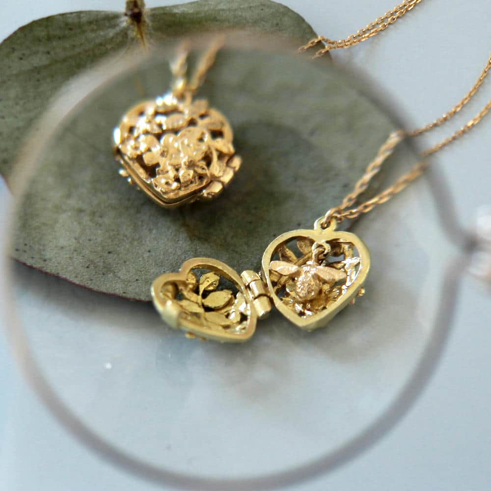 Close up of two solid 18ct yellow gold, floral detailed heart shaped locket necklaces containing a tiny bee.