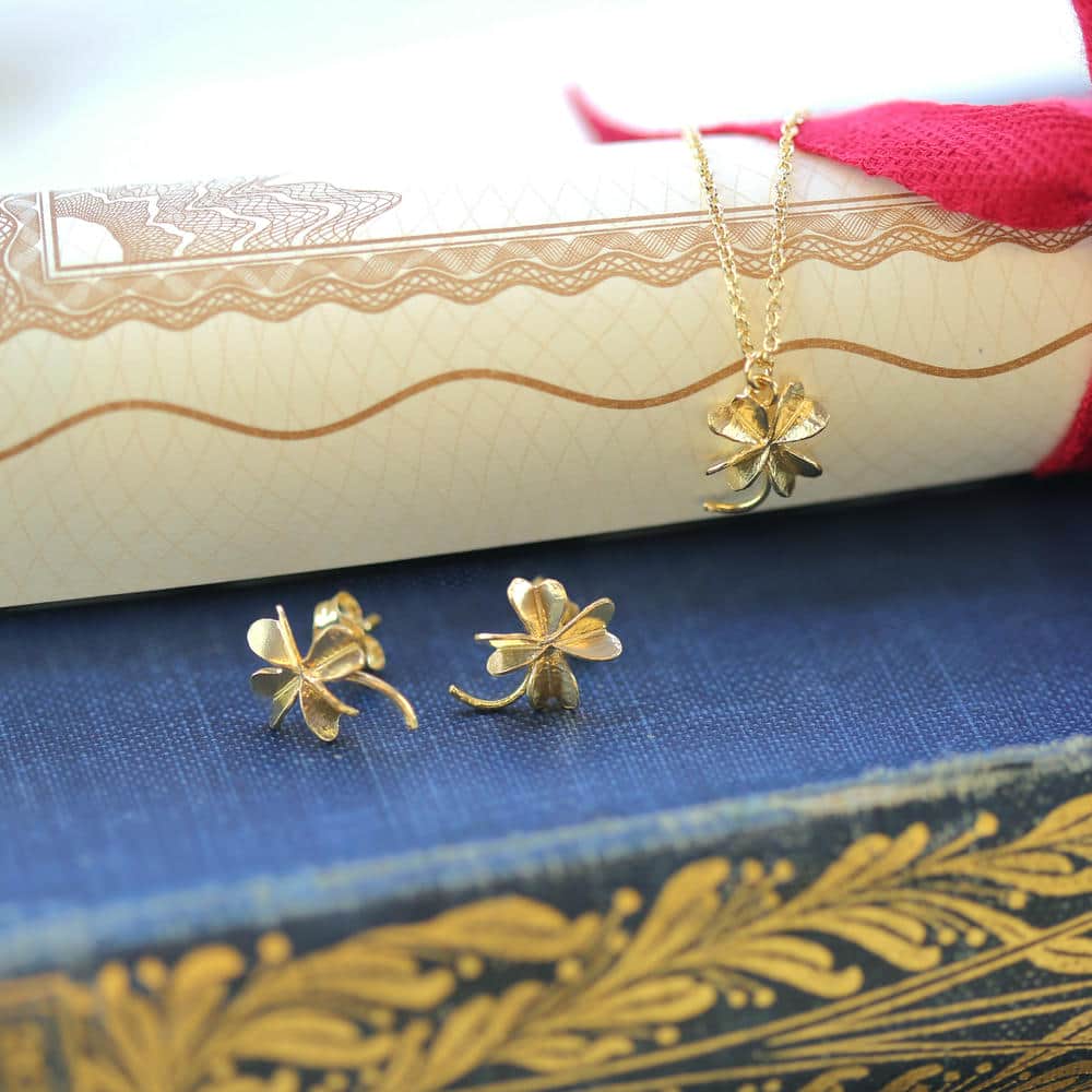 Gold four leaf lucky clover stud earrings and necklace displayed across a rolled up scroll.