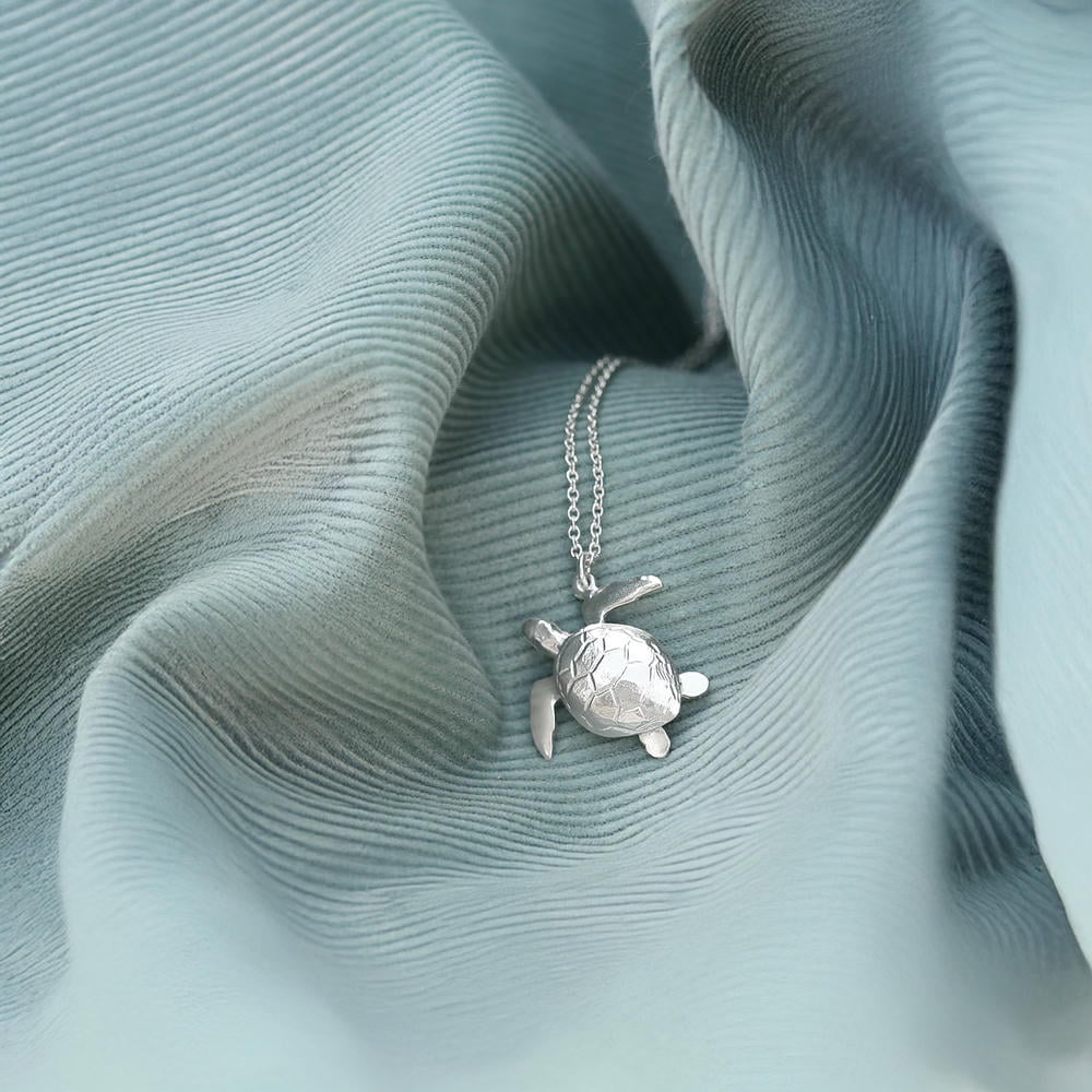 Silver turtle necklace resting on textured blue fabric