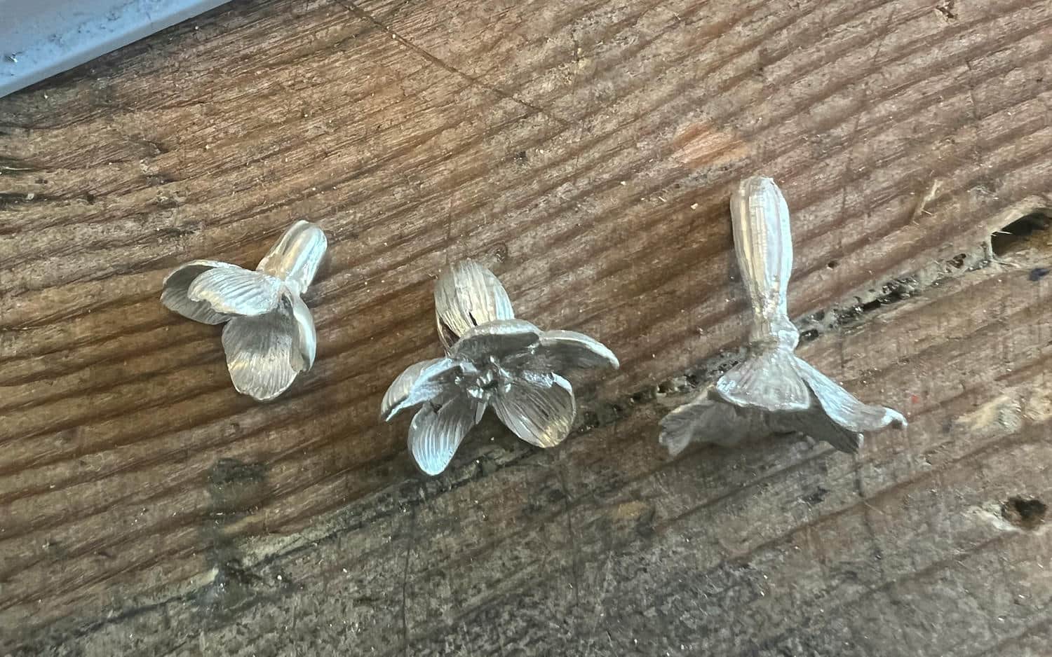 Close up of three silver flowers on a wooden surface.
