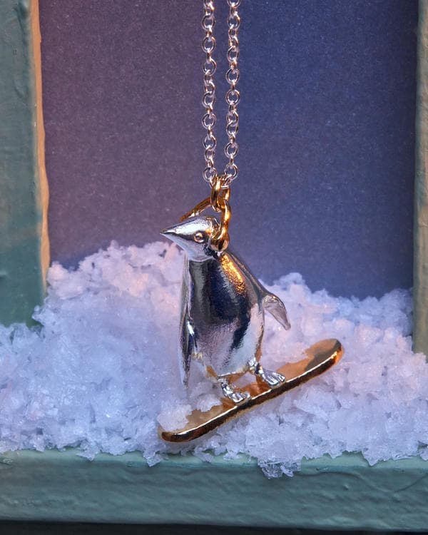 Silver penguin on a gold plated snowboard wearing earmuffs.