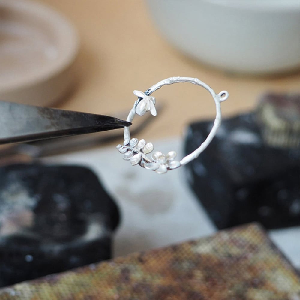 student holding up bee loop necklace with pliers at Alex Monroe 's jewellery school class