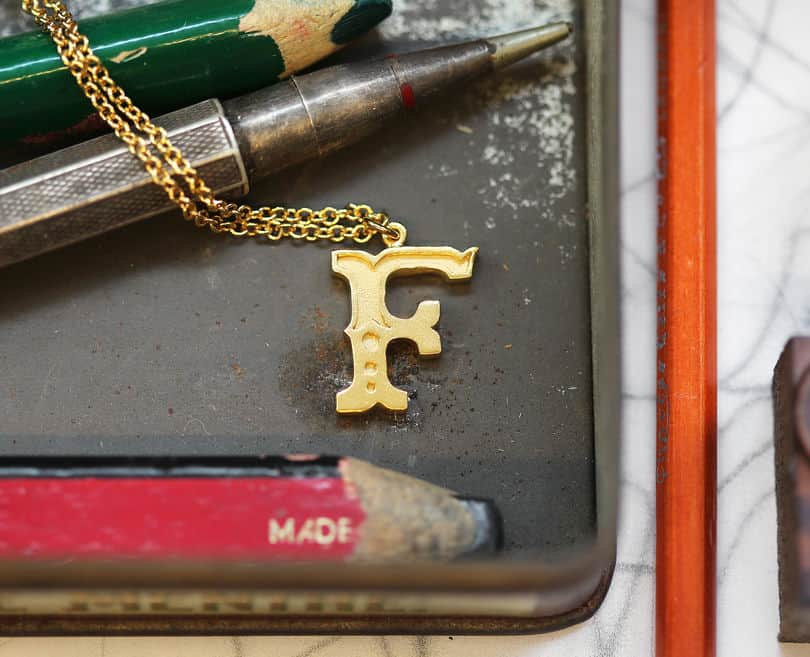 Alex Monroe's Letter F necklace placed of a black paint pallet