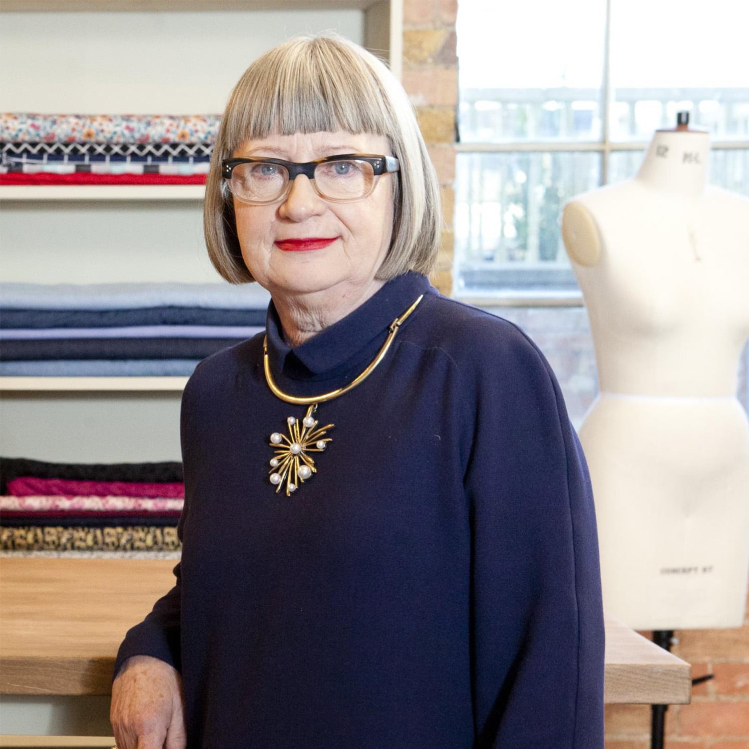 Profile photo of Esme Young wearing a navy jumper and a gold statement necklace