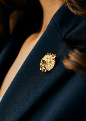 RNLI x Alex Monroe Gold Plated Coastal Scene Brooch styled with navy blazer and white top.