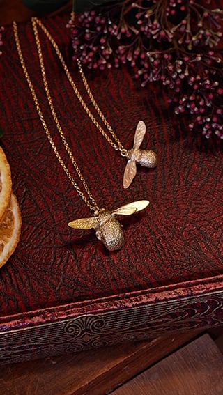 Alex Monroe's bumblebee and baby bee necklace placed on a vintage textured book