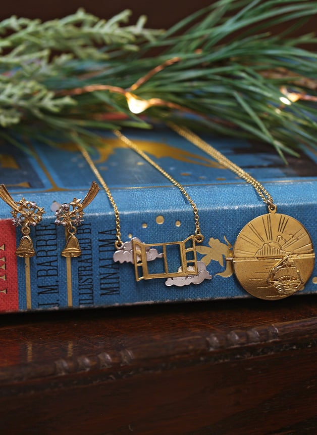 Open Window Necklace , Tinker Bell Stud Drop Earrings and Sail into the Sunset Folding Disc Necklace sitting on peter pan by Alex Monroe Jewellery