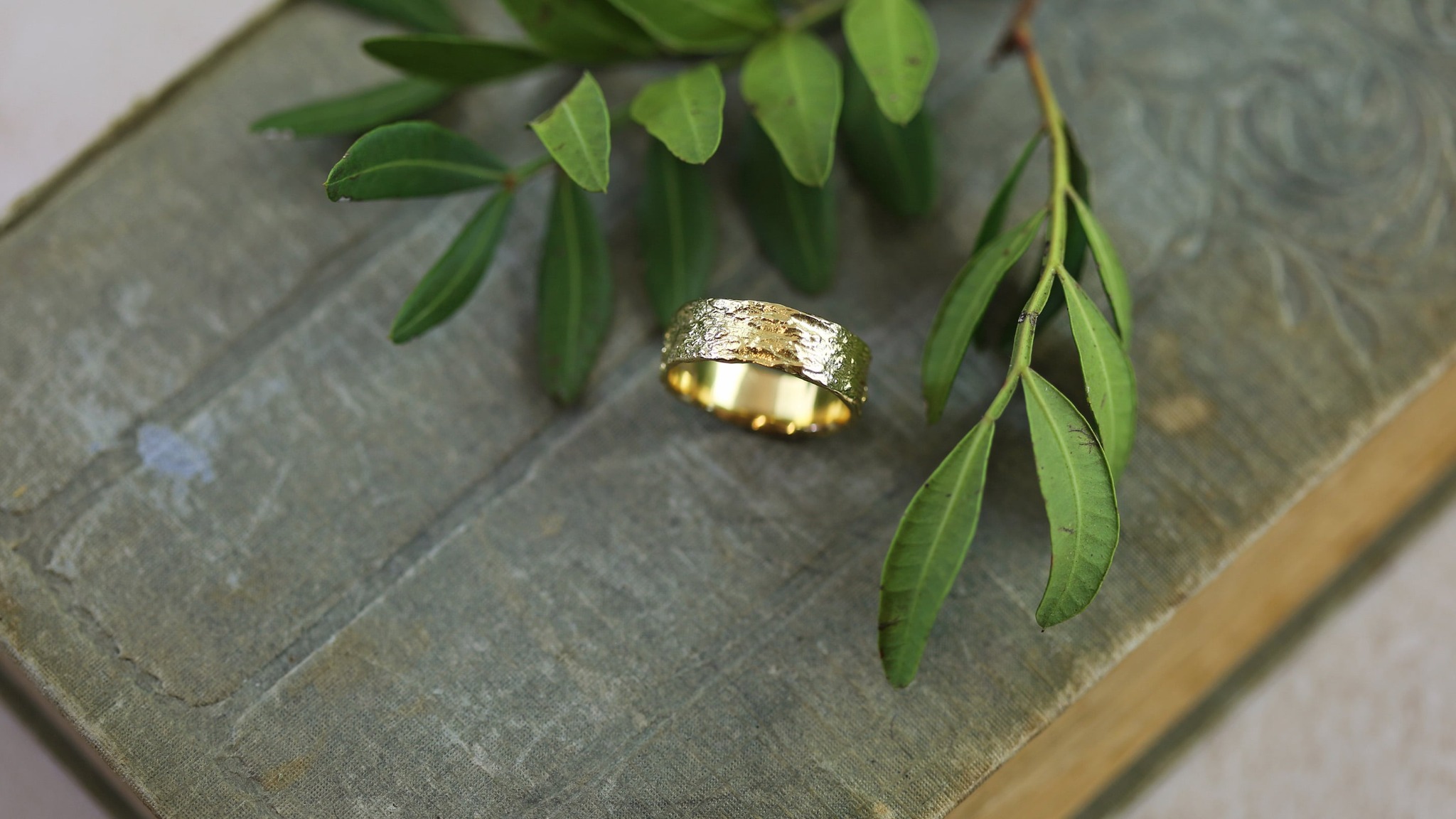 Wide bark textured 18ct Solid Yellow Gold wedding ring placed on a vintage book, with a green leaf
