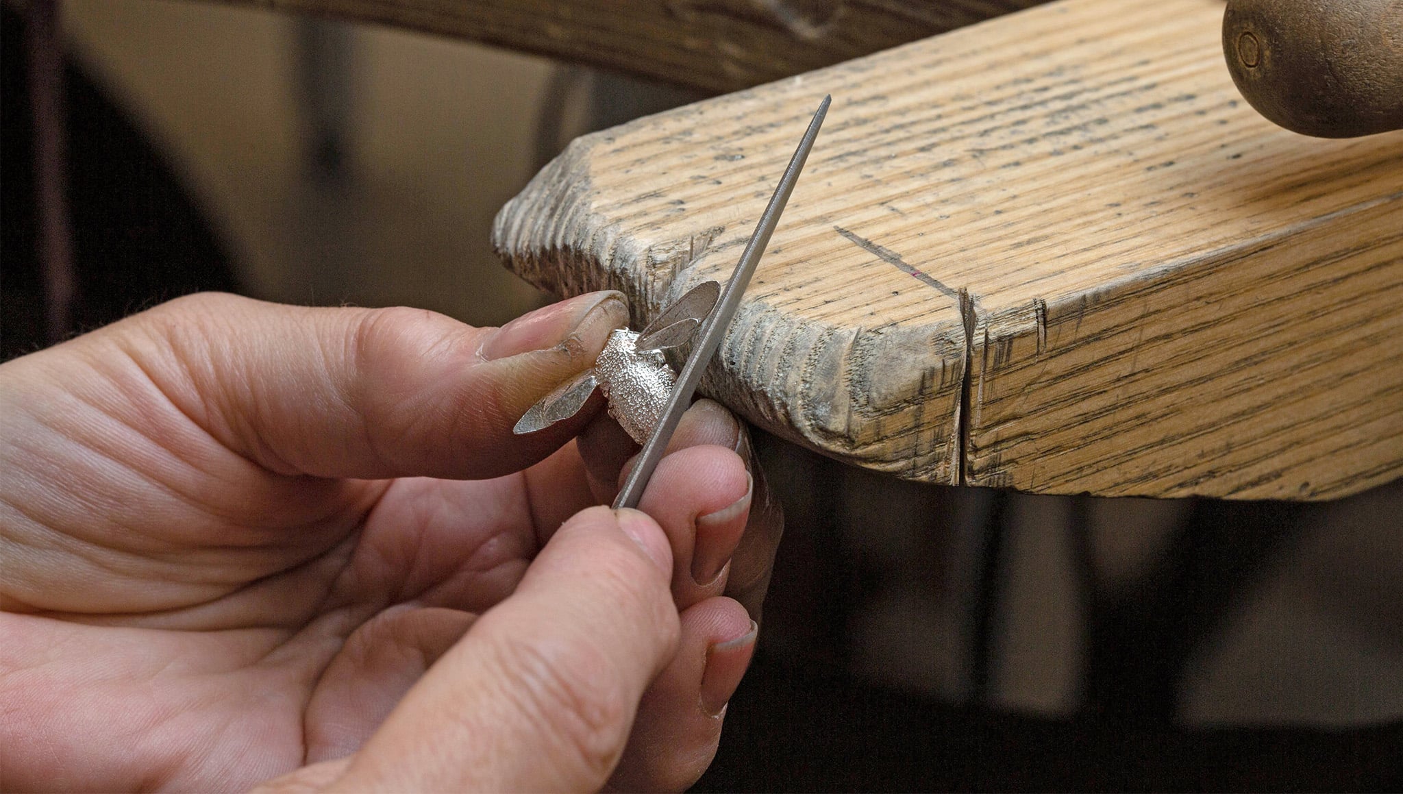 Workshop image of a silver bumblebee necklace casting being filled down on a jewellers bench