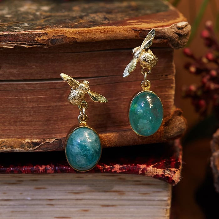 18ct one of a kind emerald and bee drop earrings, hanging from a vintage book