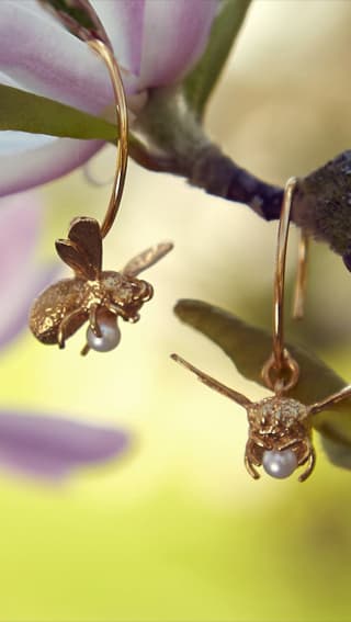 Gold plated flying bee with pearl earrings hanging from a flower