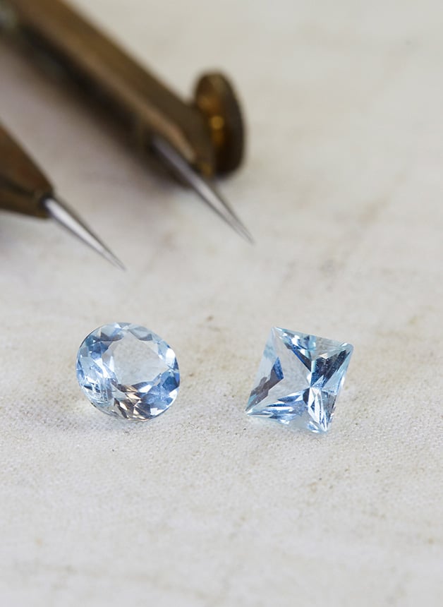 2 shiny aquamarine gemstones sitting on a cream textured canvas fabric