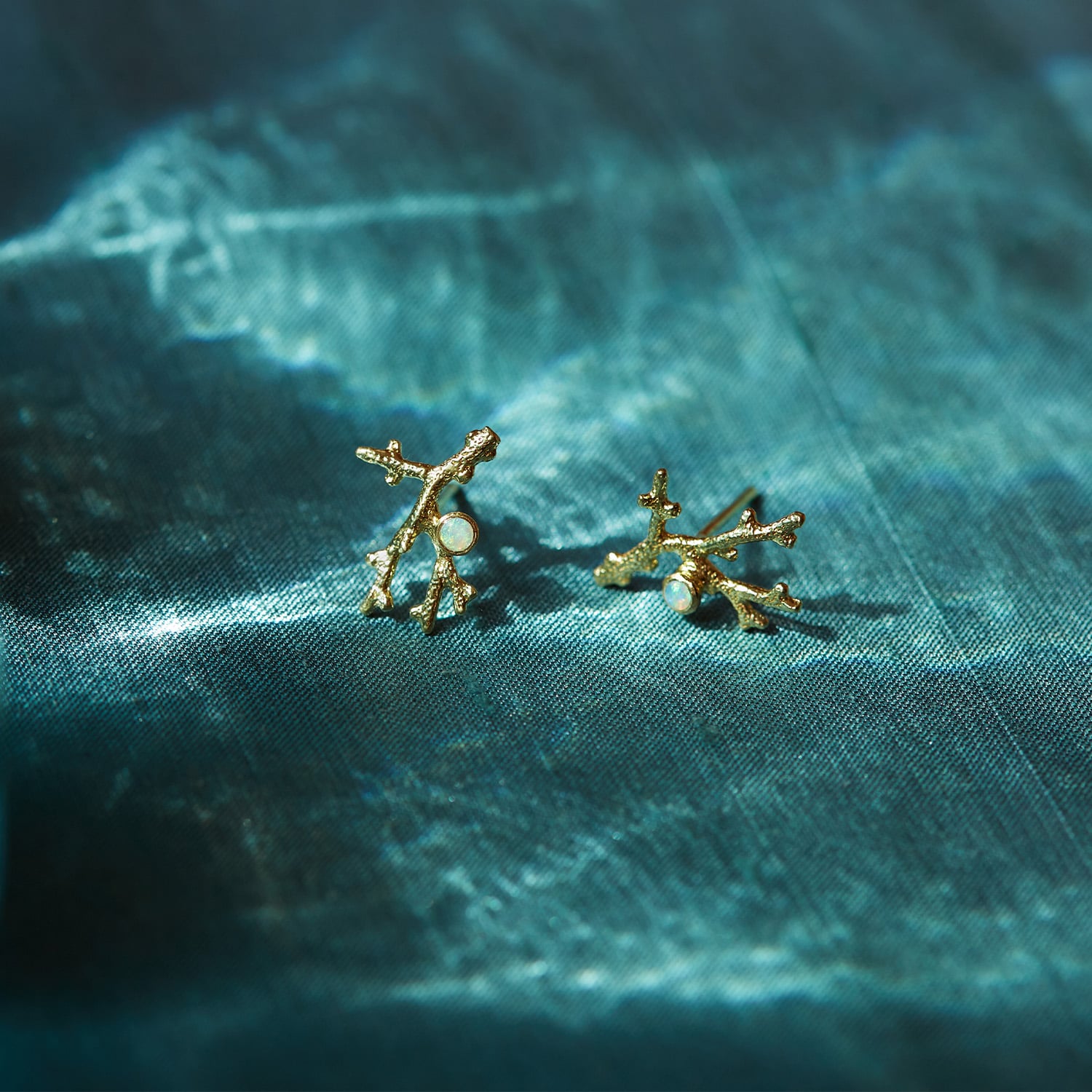 Coral Branch Stud Earrings with Opal placed on top of a dark blue fabric by Alex Monroe Jewellery