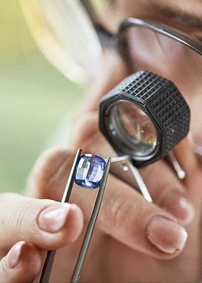 Inspecting a large blue sapphire gemstone with a jewellers loupe.