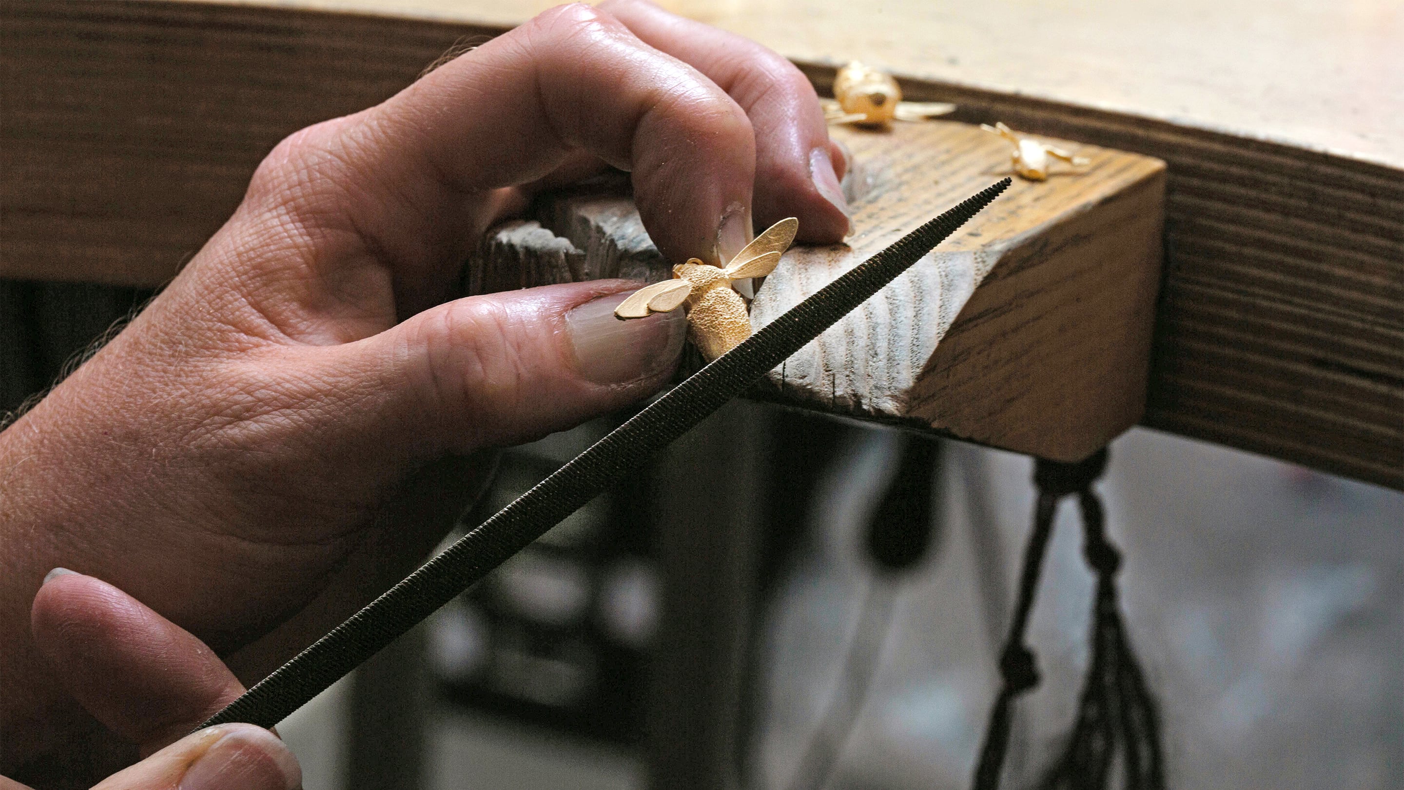 Jeweller in the workshop using a file to finish a bumblebee casting at the jewellers bench.
