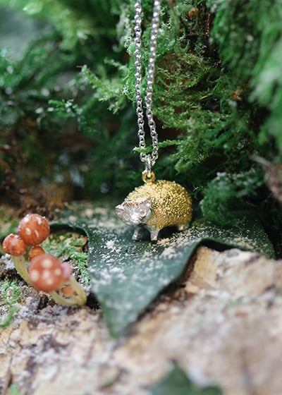 hedgehog necklace on a green leaf, surrounded by a green forest