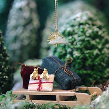 Honey Bee Stud Earrings on a pile of presents on a small wooden sleigh surrounded by snow covered trees and below a sunray and cloud necklace
