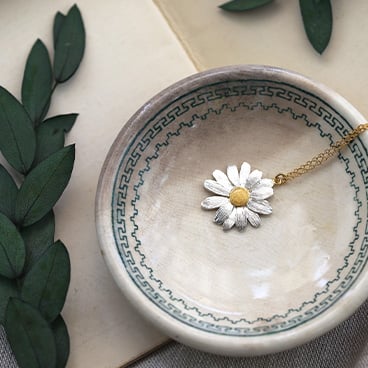 A large mixed metal daisy necklace placed on top of a bunch of white flowers