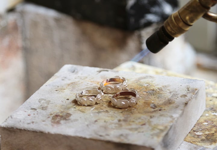 Using tweezers to hold an 18ct yellow gold ring casting on the forge whilst using a blow torch to heat the casting.