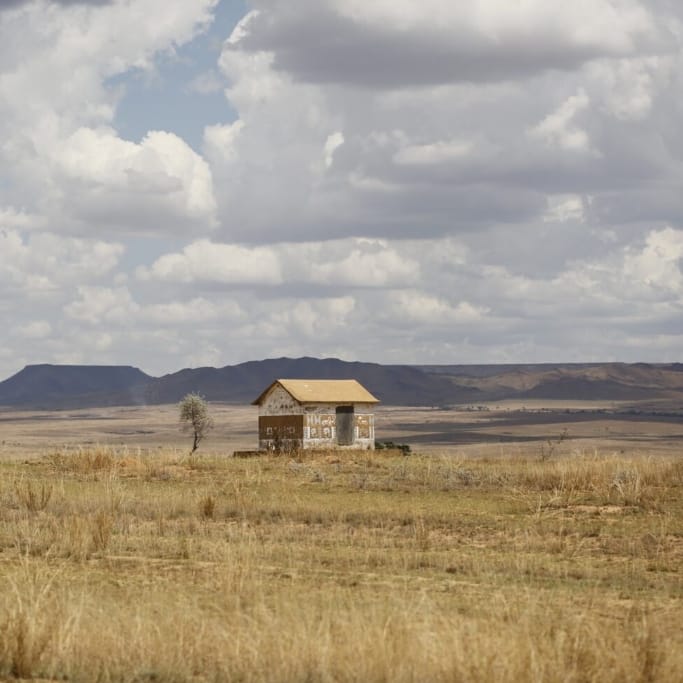 Small building in the middle of a flat plain covered with yellow grasses.