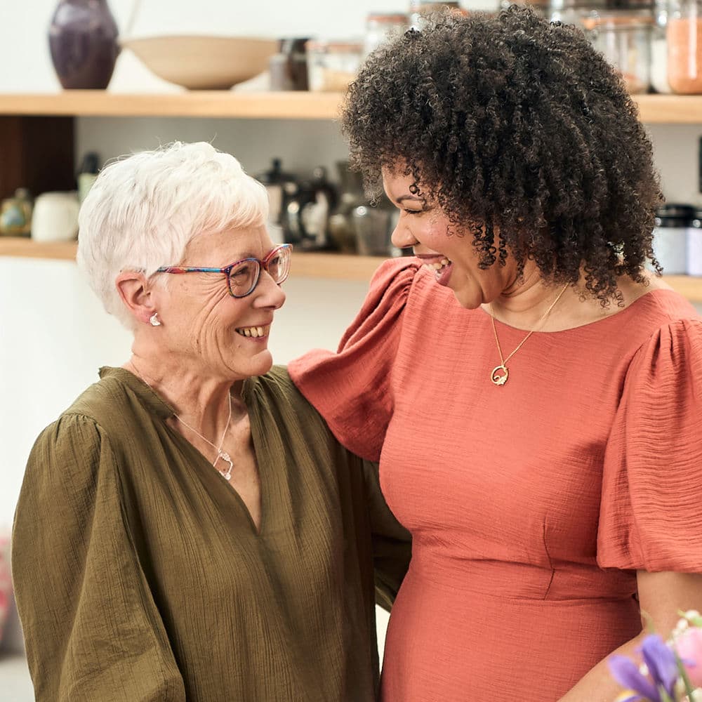 Jan and Naomi hugging, wearing their Alex Monroe Jewellery School Necklace creations.