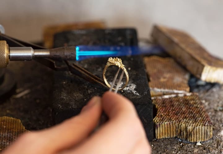 Using tweezers to hold an 18ct yellow gold ring casting on the forge whilst using a blow torch to heat the casting.