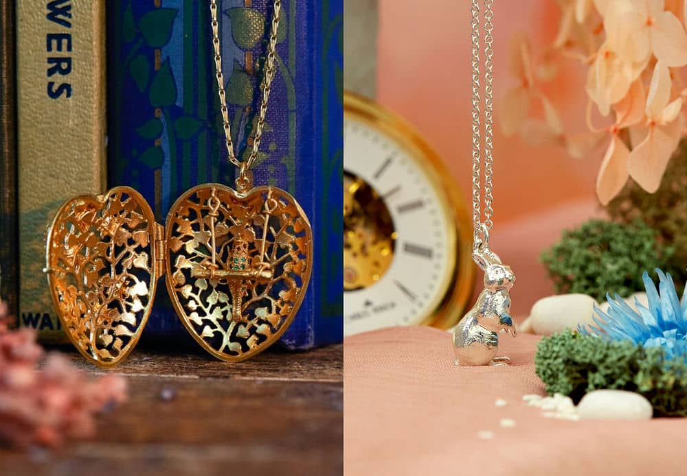 Large heart shaped locket containing a parrot on a swinging perch, set with colourful gemstones. Silver Rabbit necklace from Alice in Wonderland collection displayed with an oversized pocketwatch in the background.