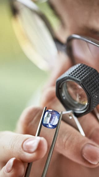 Inspecting blue sapphire gemstone with jewellers loupe.