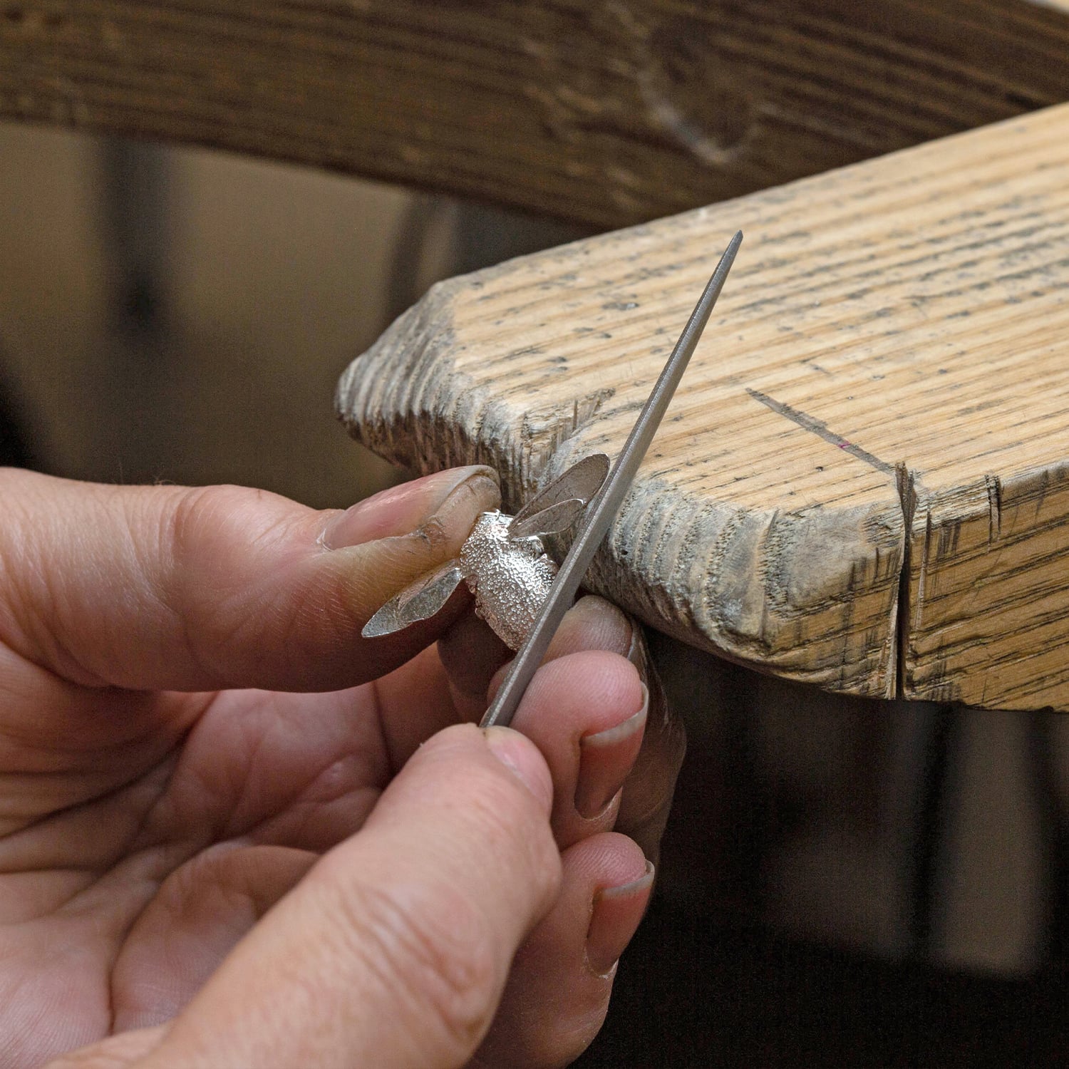 Hand making an Alex Monroe silver bumblebee necklace on a jeweller's bench with metal file