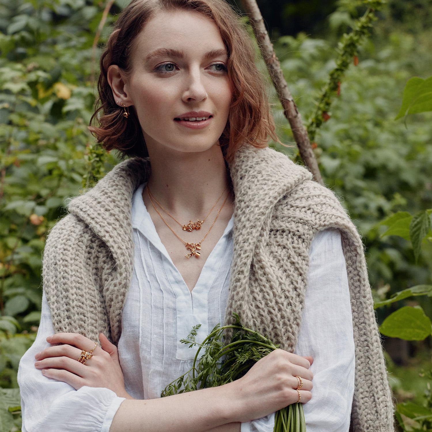 Model wearing gold plated Inline Allotment and Award Winning Radish Necklace by Alex Monroe Jewellery holding a bunch of carrots