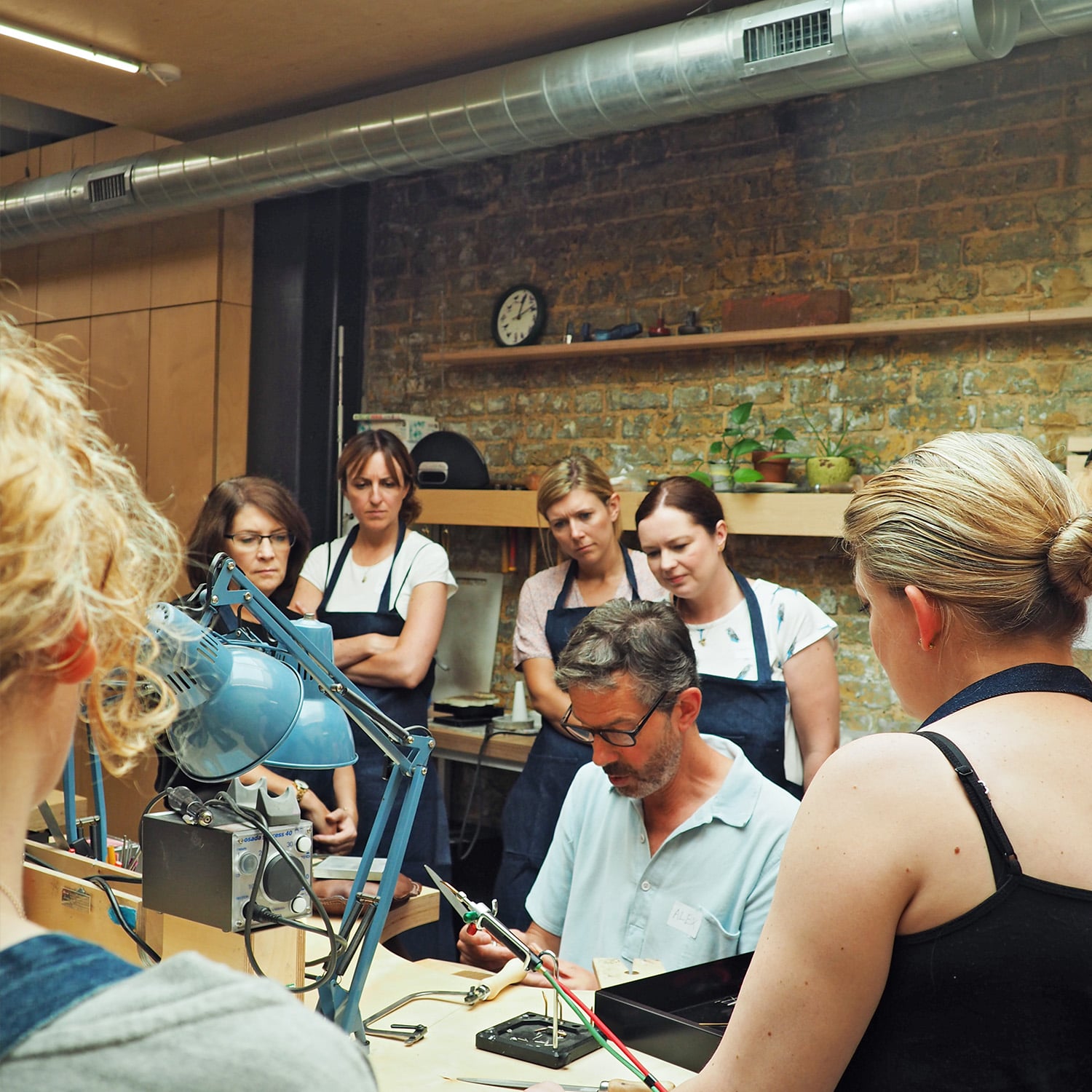 Alex Monroe showing Jewellery schoolers how to use workshop tools before they begin making